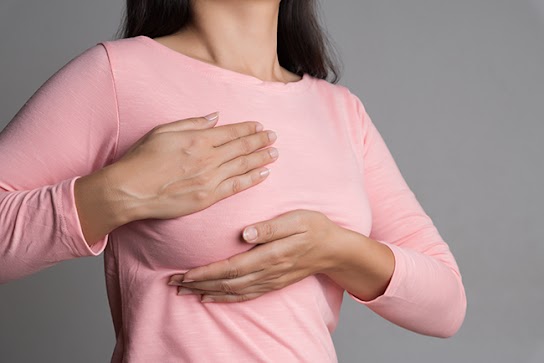 Woman hand checking lumps on her breast for signs of breast cancer on gray background. Healthcare concept. The Home Doctor Book Guide